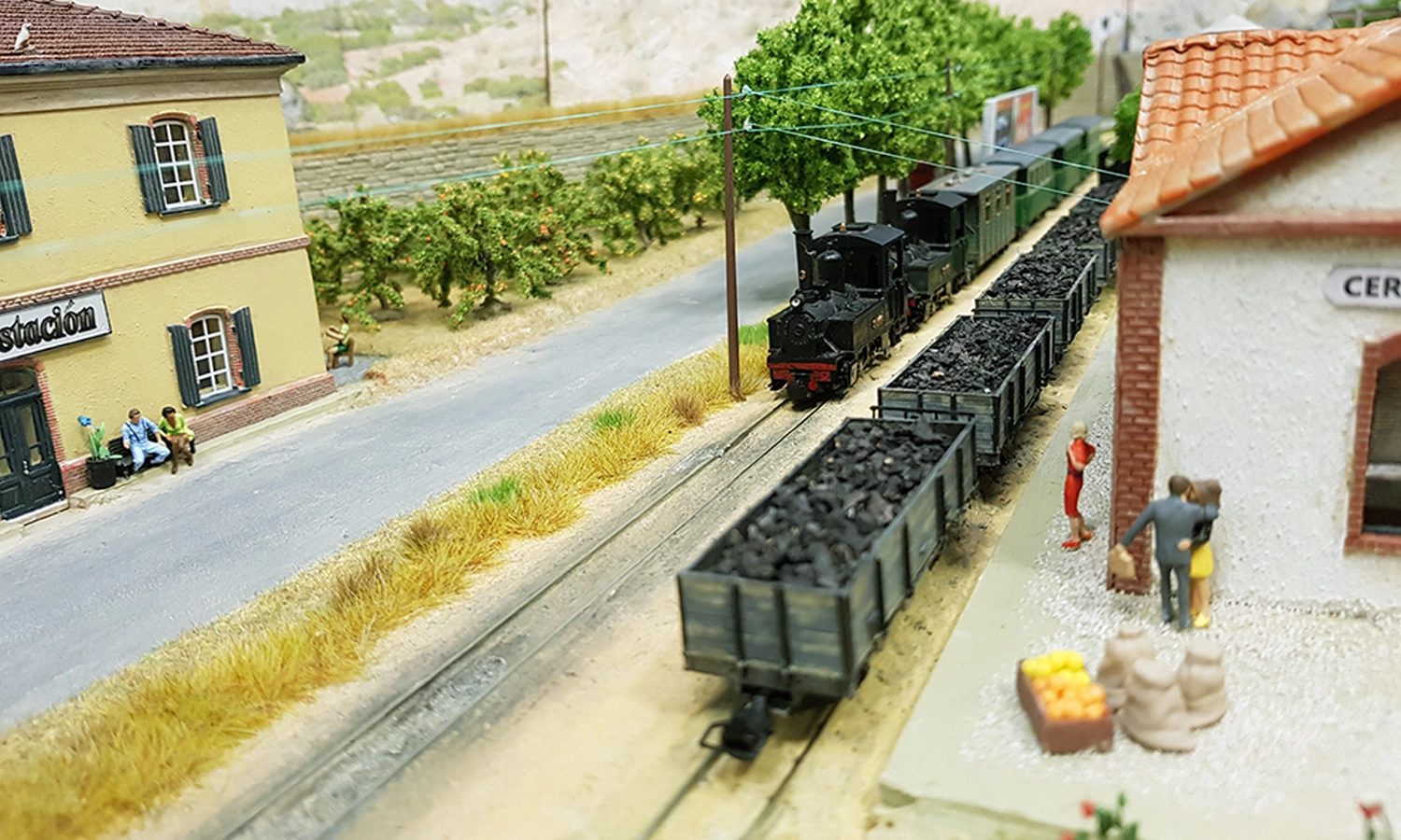 Click To Enlarge. A simple, straight model railway track is surrounded by green trees and hills in the Spanish countryside.