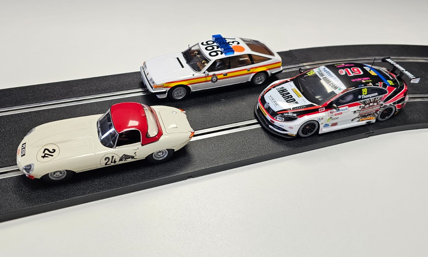 A length of slot car race track displaying three different Scalextric slot cars from over the years.