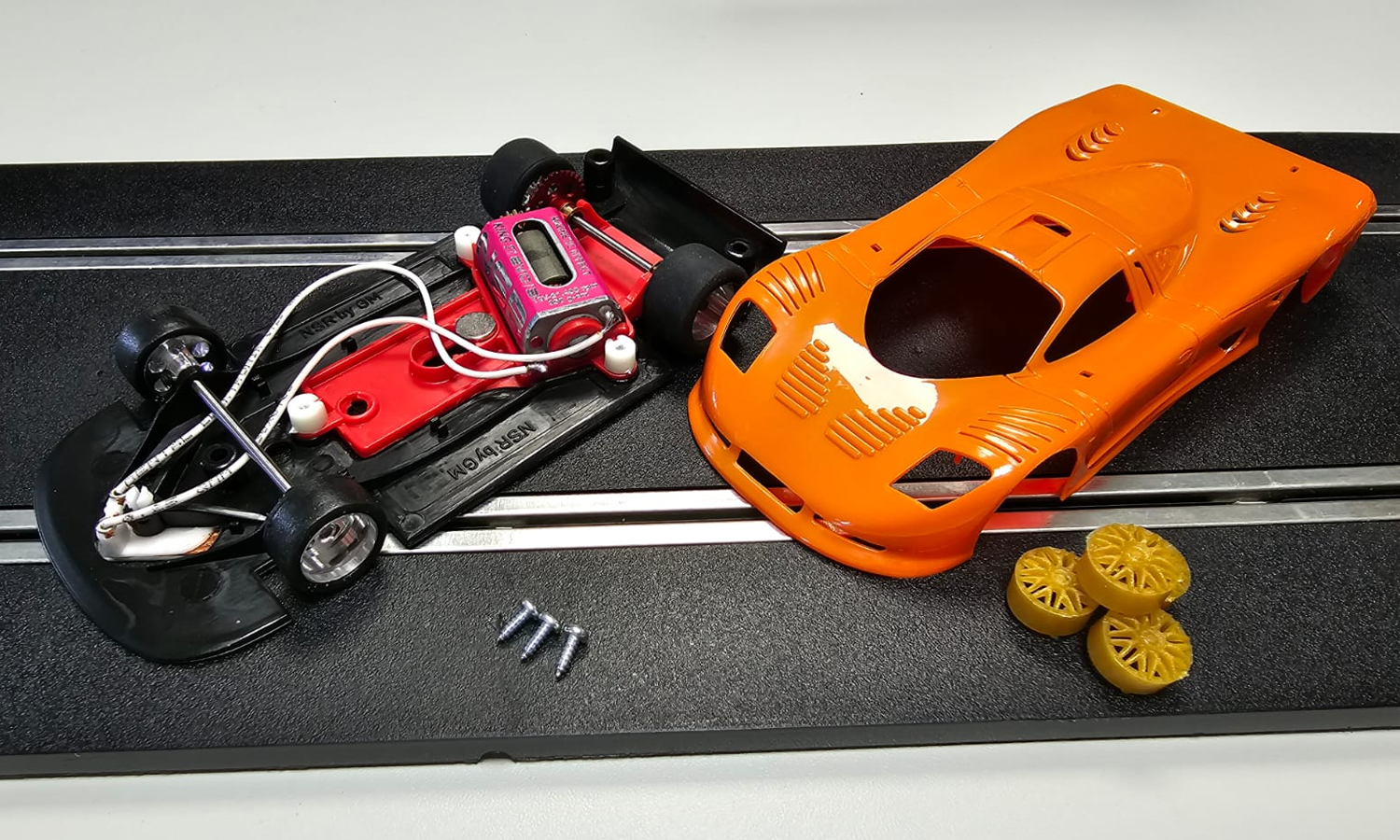 A deconstructed slot car from a customisable kit, laid out on a piece of slot car race track.